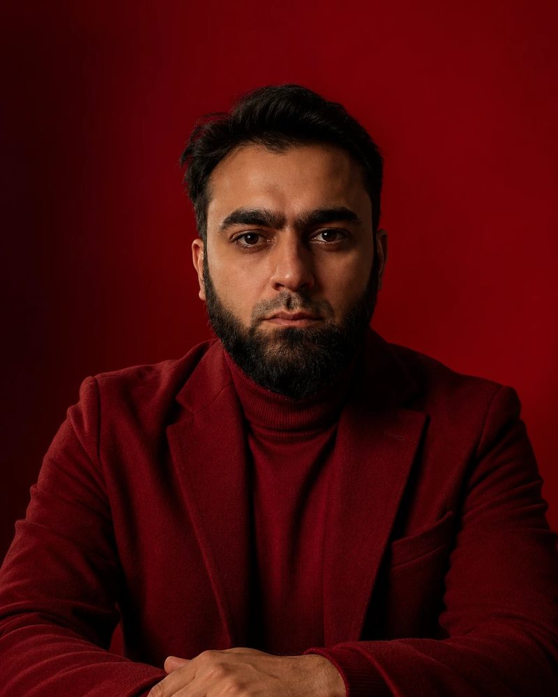 Portrait of Asfand Yar Junejo in a red blazer and turtleneck against a red backdrop