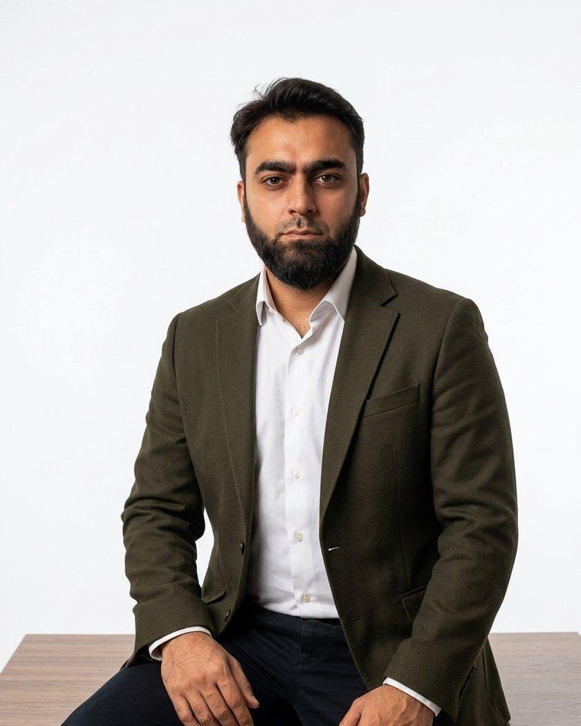 Asfand Yar Junejo, AI Search Visibility and AEO Strategist, seated on a wooden desk in an olive blazer